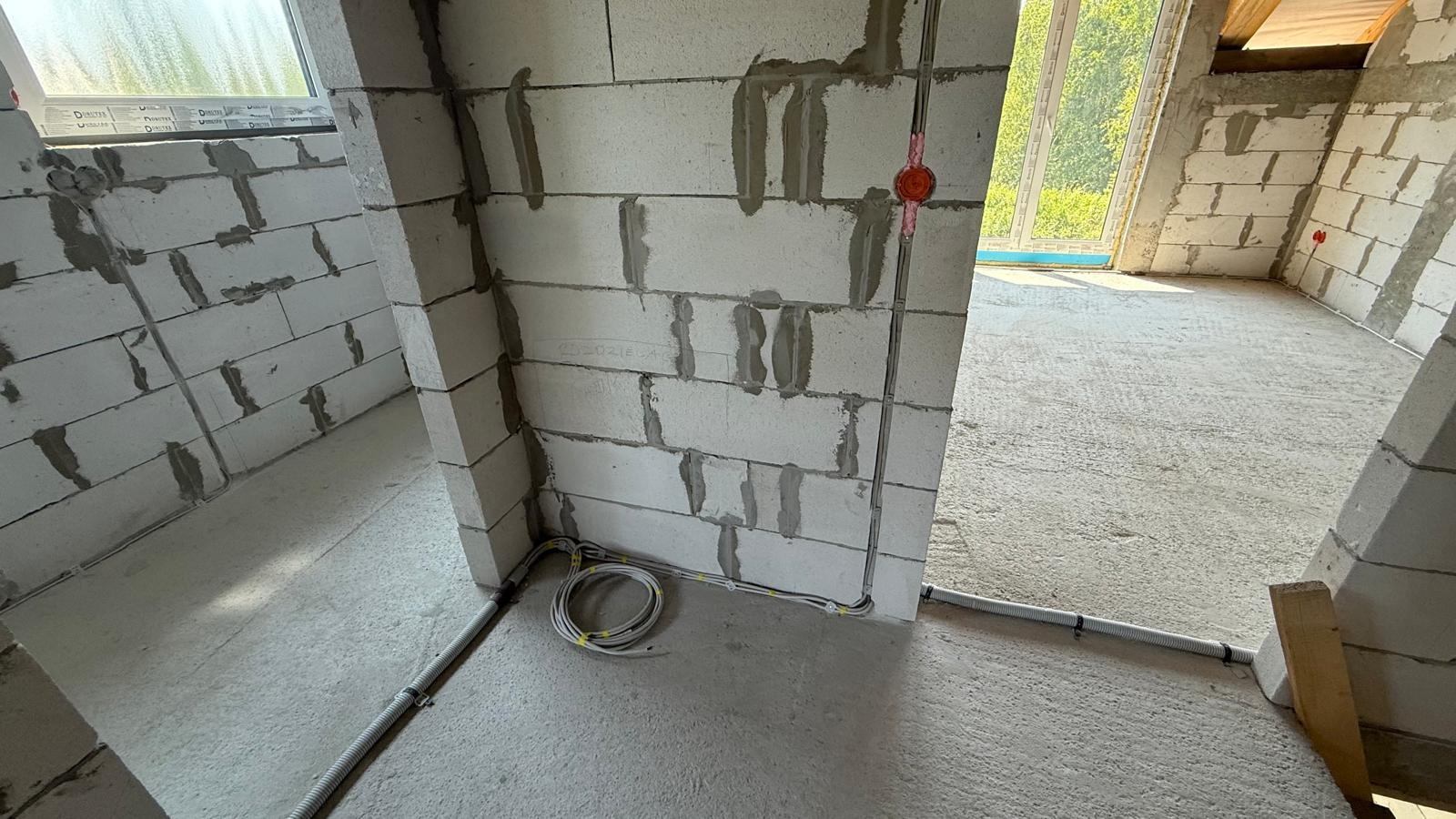 Surowy stan: przewody elektryczne w ścianach z betonu komórkowego, okrągła puszka instalacyjna, przewody ułożone na podłodze. W tle okno i surowe ściany.