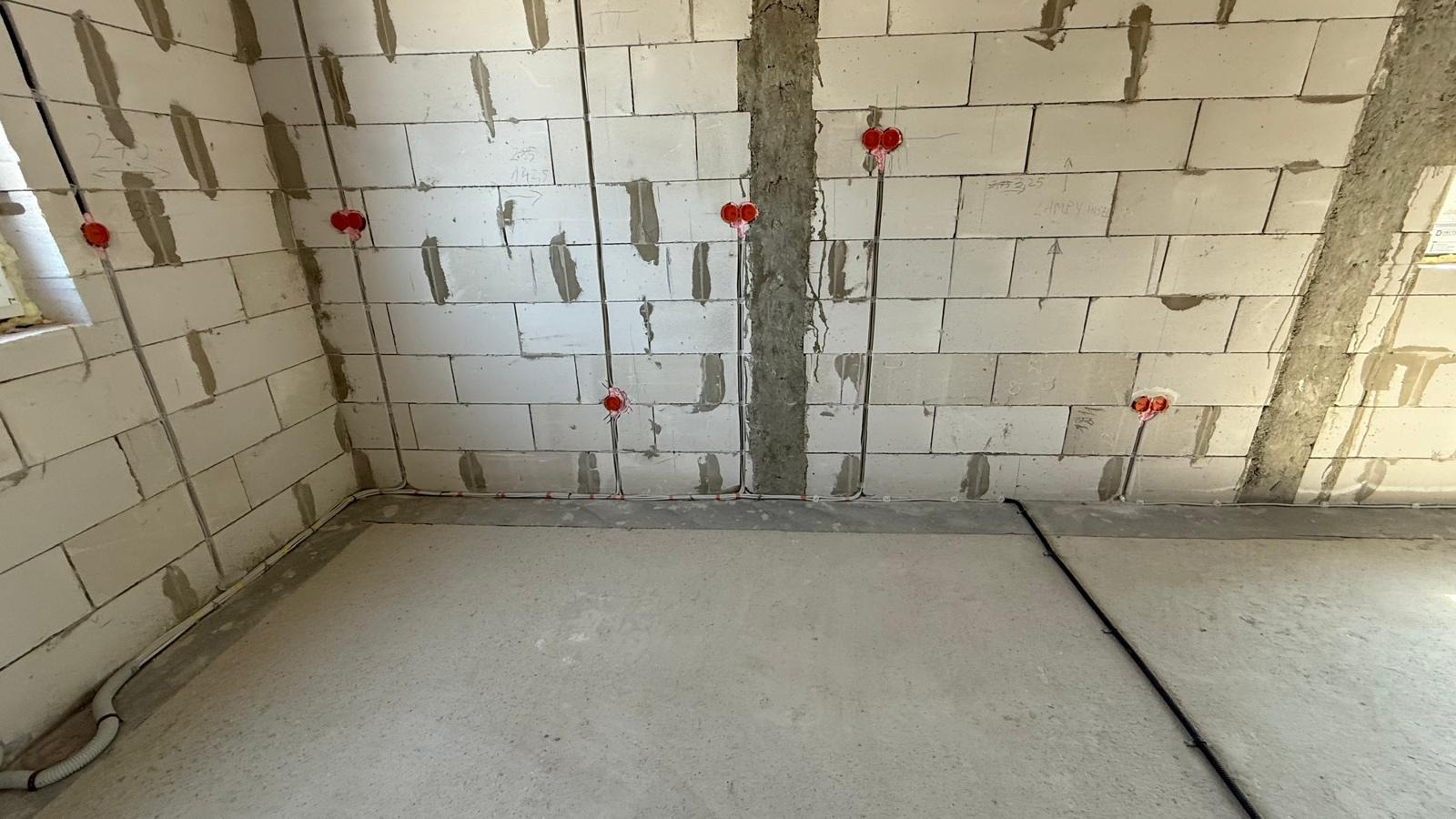 Wnętrze w trakcie prac elektrycznych: widoczne kable w ścianach z betonu komórkowego i w podłodze, przygotowane punkty instalacyjne z puszkami w kolorze pomarańczowym.