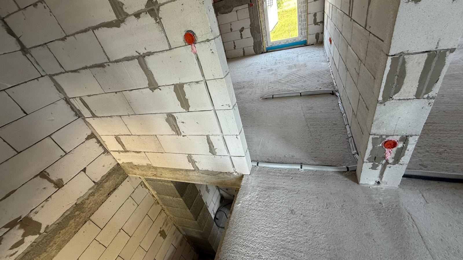 Wnętrze w trakcie budowy z widocznymi przewodami elektrycznymi w peszlach, zamontowanymi na ścianach z bloczków betonowych. Widoczne puszki elektryczne.