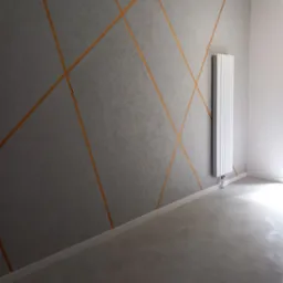 Szara ściana z dekoracyjnymi, pomarańczowymi liniami, grzejnikiem i jasną podłogą w pustym pokoju.