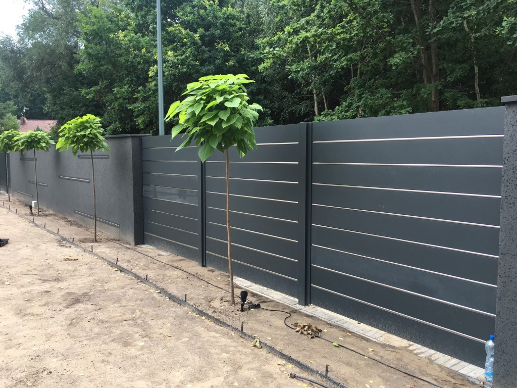 Nowoczesne, poziome, grafitowe panele ogrodzeniowe z metalowymi akcentami, oddzielające posesję, z młodymi drzewkami wzdłuż ogrodzenia