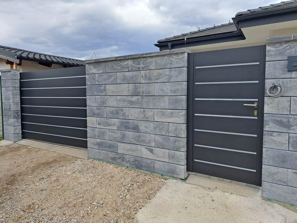 Nowoczesna brama przesuwna i furtka z poziomymi panelami, szara kostka betonowa na słupkach i murku, widoczne elementy instalacji elektrycznej przy furtce.