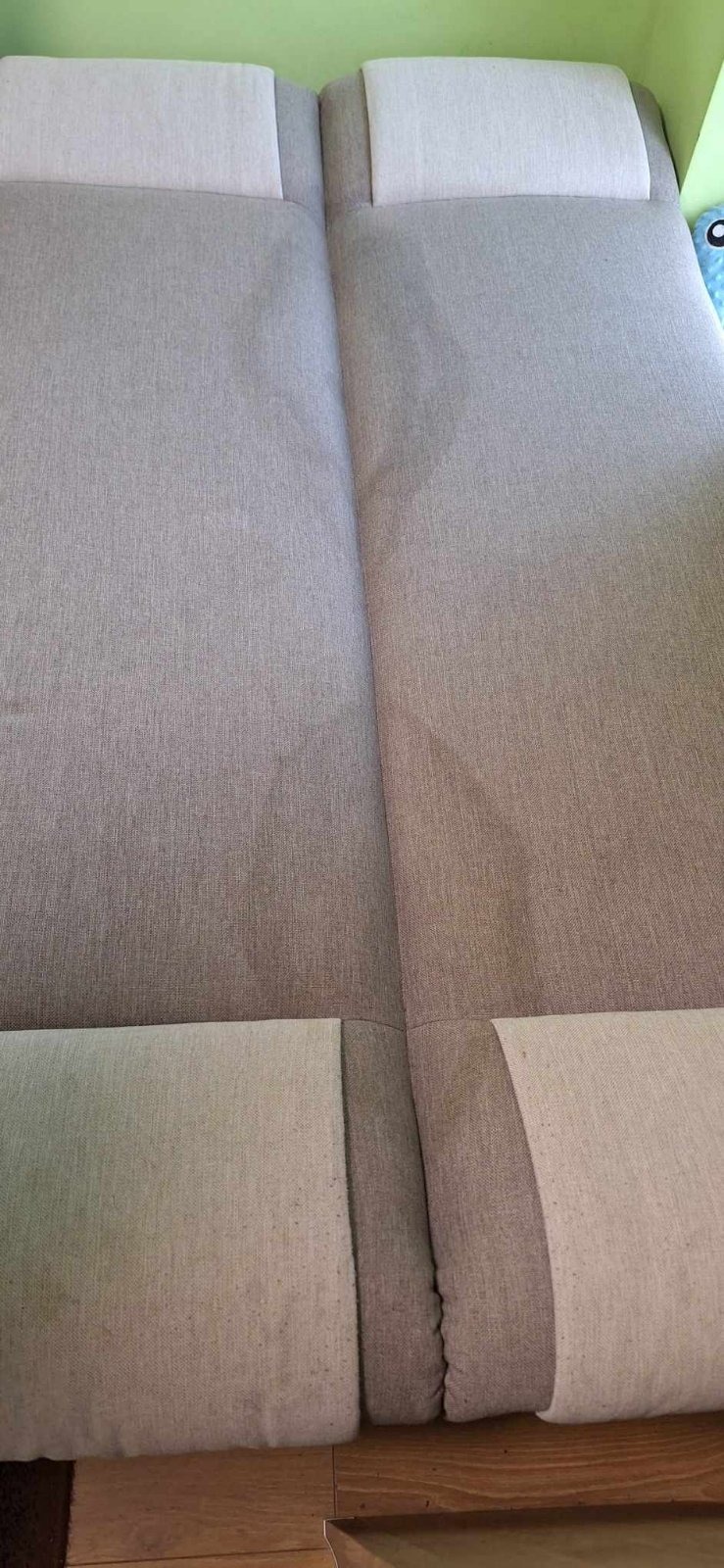 Fragment szarej, rozłożonej kanapy z jasnymi zagłówkami, widoczny ślad po czyszczeniu na jednym z segmentów.