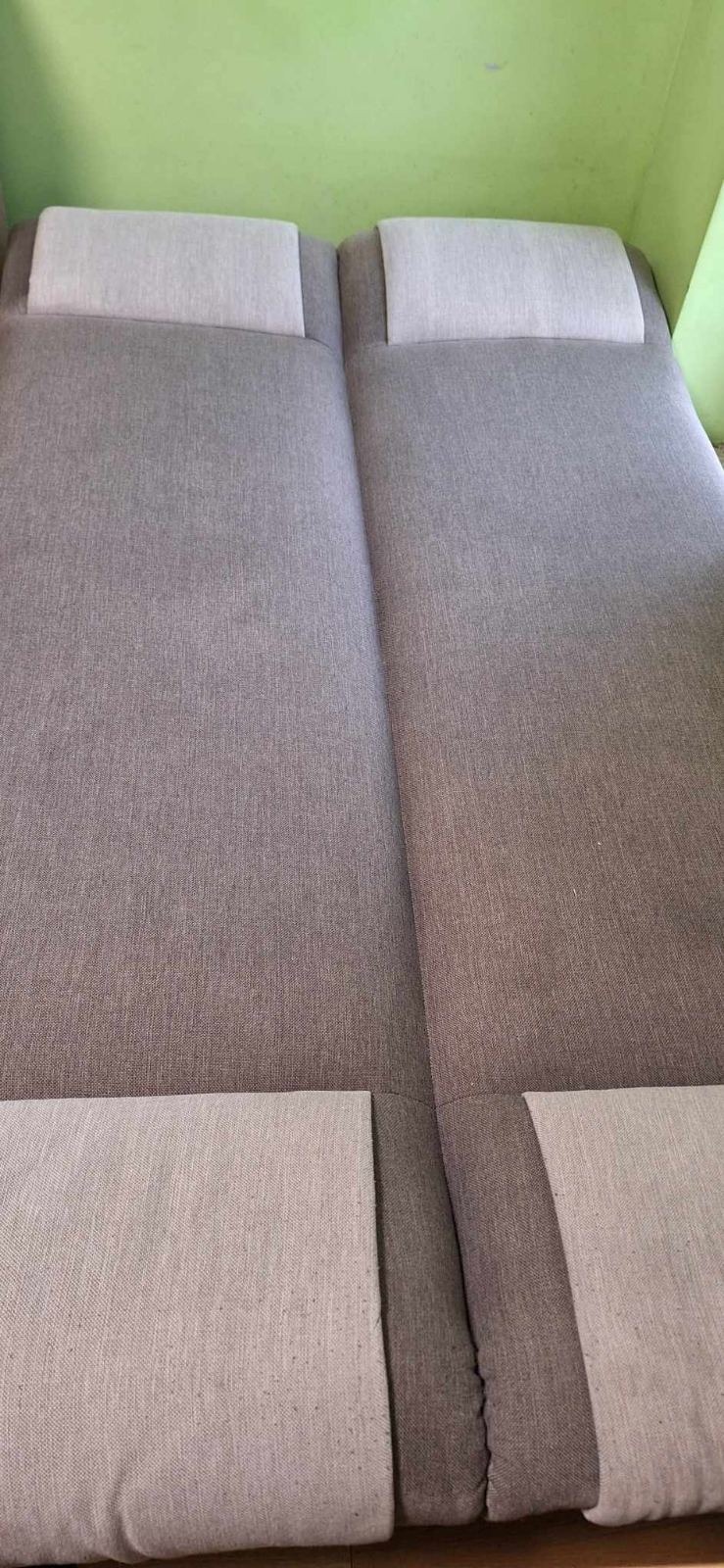 Szary, rozłożony narożnik z jasnymi zagłówkami na tle zielonej ściany.