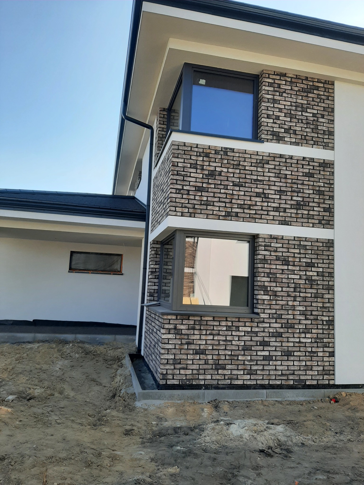 Dwukondygnacyjny budynek w Gliwicach z elewacją z cegły klinkierowej, okna z szarymi ramami i fragmentem białej elewacji, widoczne przygotowanie terenu przed budynkiem.