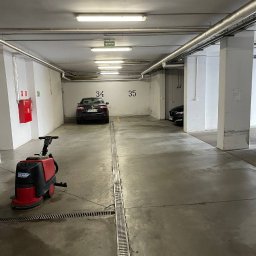 NOVA CLEAN VITALII TSYTSYLIN - Czerwono-czarna maszyna czyszcząca Cleanfix na betonowej posadzce parkingu podziemnego z numerami miejsc 34 i 35 w tle. Widoczne odpływy liniowe.