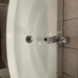 Łowca Kurzu - Biała umywalka z chromowaną baterią na tle beżowych płytek, widok z góry.