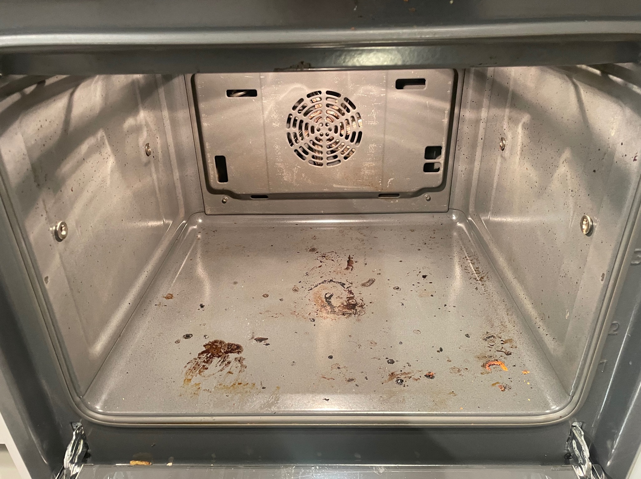 Wnętrze brudnego piekarnika ze śladami przypalonych resztek jedzenia na dnie i ściankach, widoczny element grzewczy z tyłu.