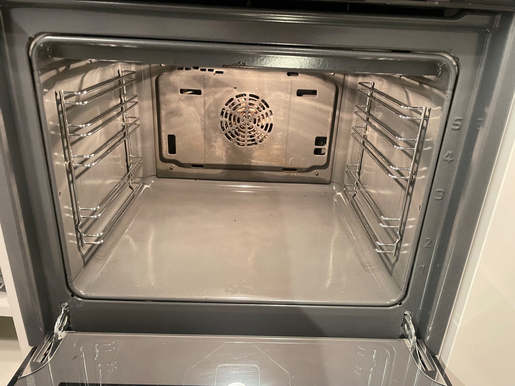 Wnętrze brudnego piekarnika z widocznymi śladami przypalenia na tylnej ściance i grzałce, z otwartymi drzwiczkami i metalowymi prowadnicami na blachy.