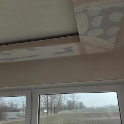 SUFITY - MP MARIUSZ PACZKOWSKI - Sufit z widocznymi łatami po szpachlowaniu, przygotowany do dalszych prac wykończeniowych, okno z widokiem na pole i drzewa w tle.