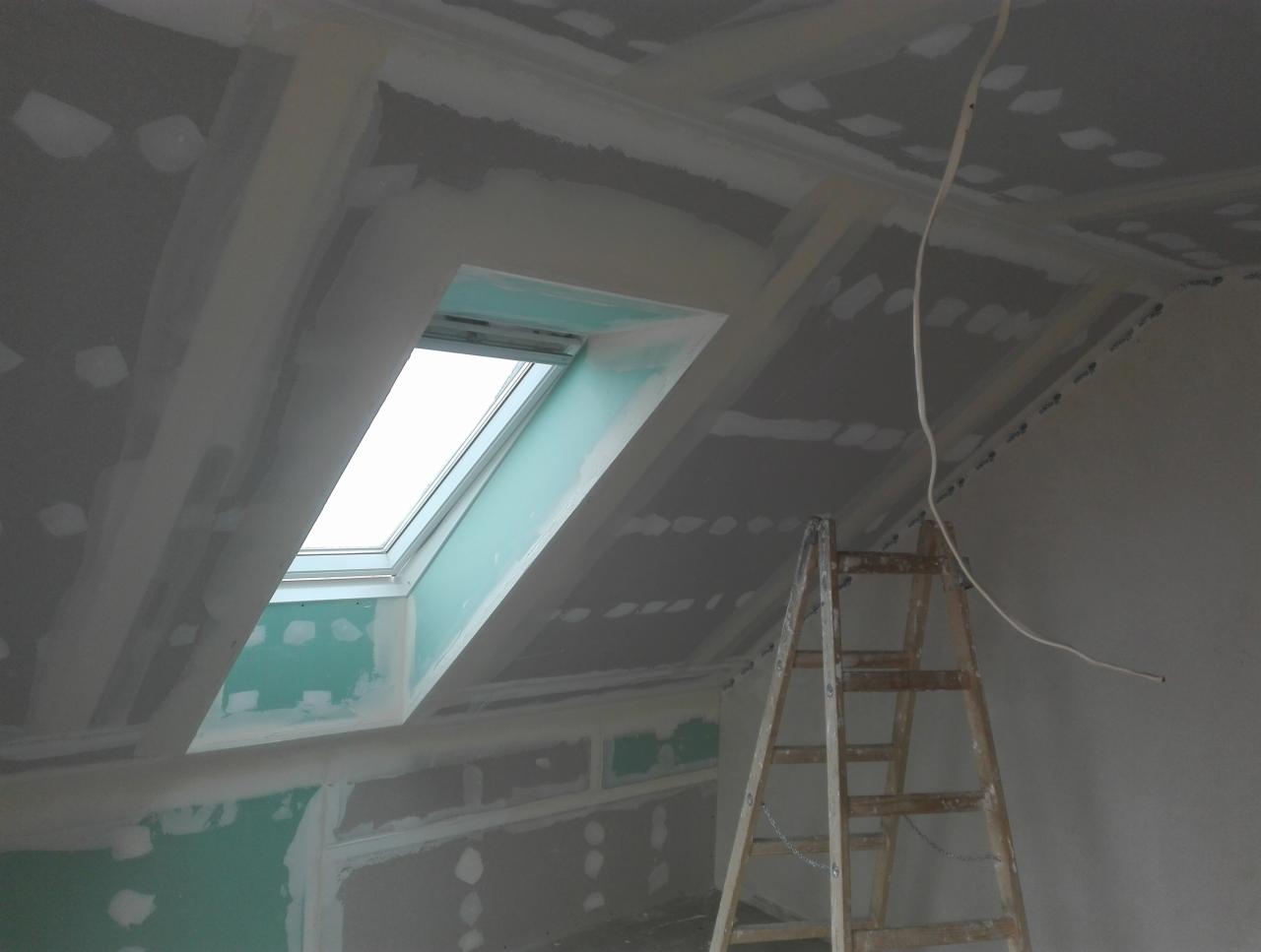 Montaż płyty karton gips na poddaszu z oknem dachowym, widoczna drewniana drabina i przewody elektryczne.