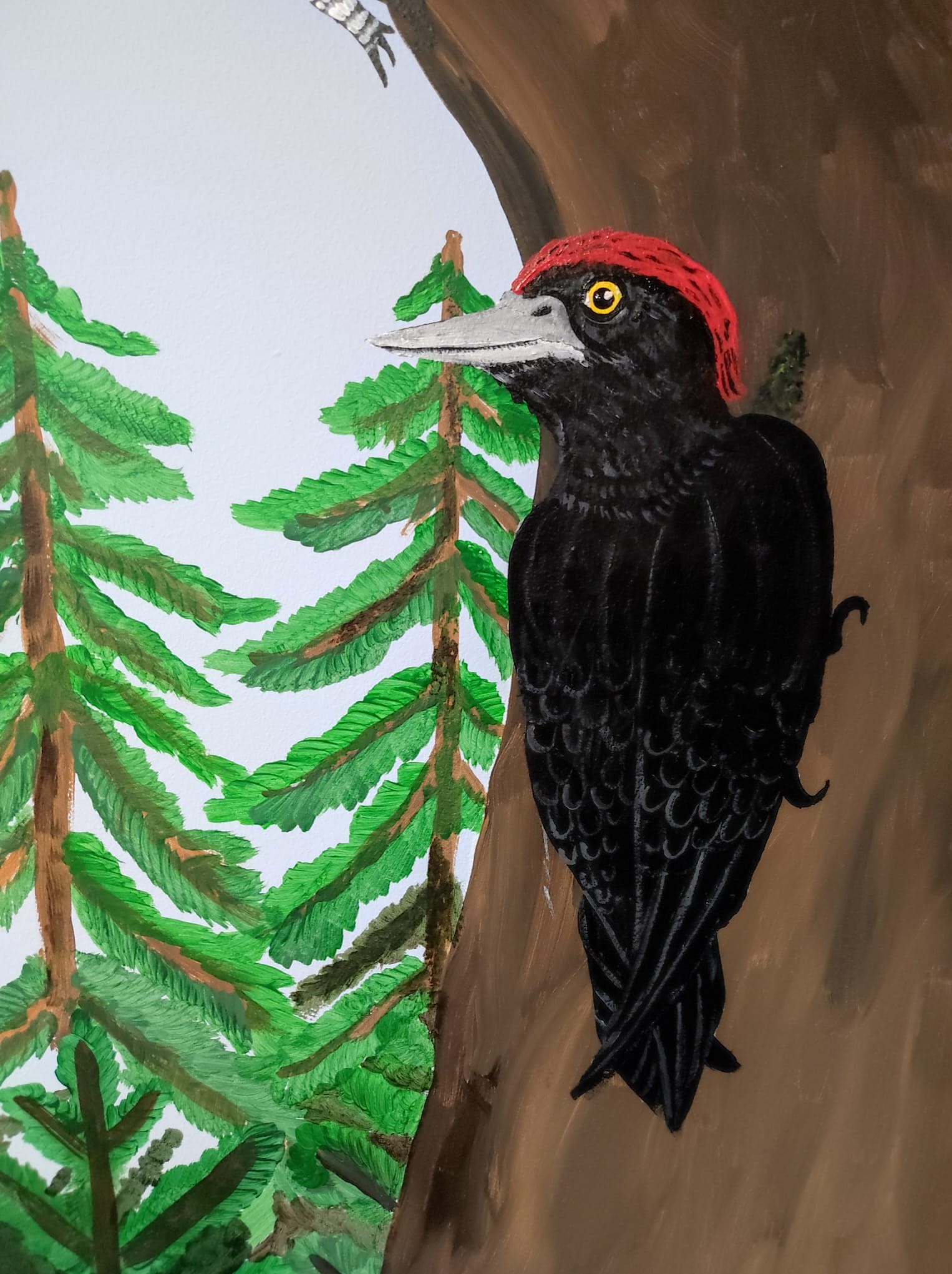 Ręcznie malowany obraz przedstawiający czarnego dzięcioła z czerwonym czubem na brązowym pniu drzewa, obok zielone drzewa iglaste na jasnym tle.