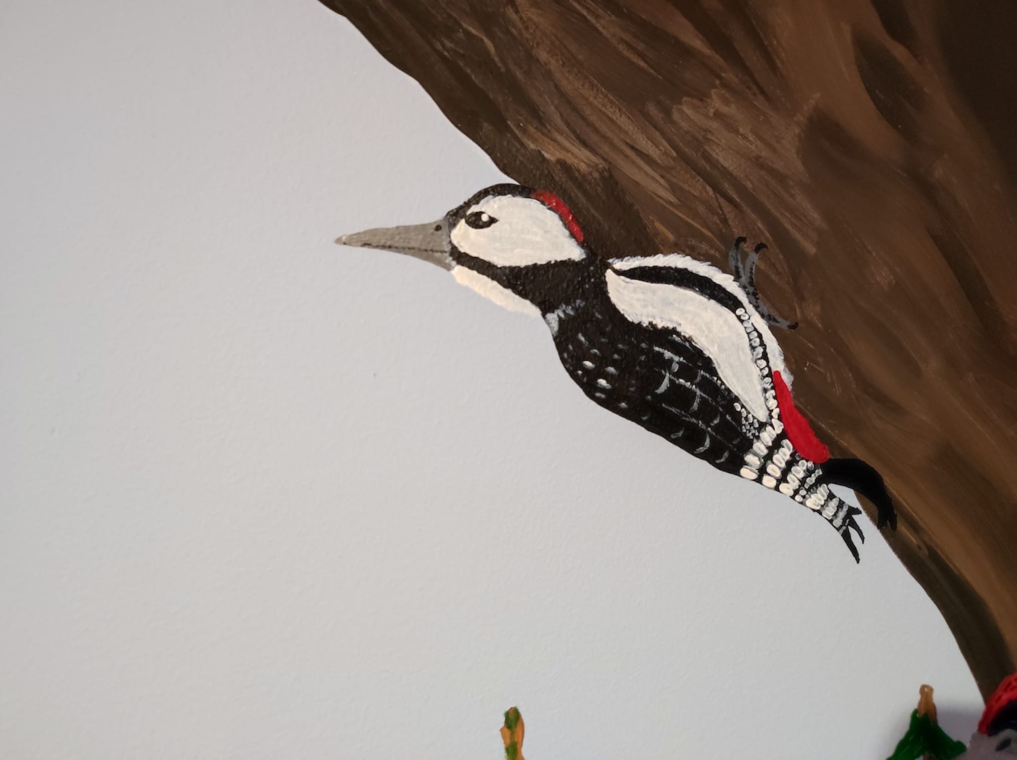 Mural przedstawiający dzięcioła dużego na brązowym pniu drzewa, z widoczną fakturą farby i elementami dekoracyjnymi w dolnej części kadru.