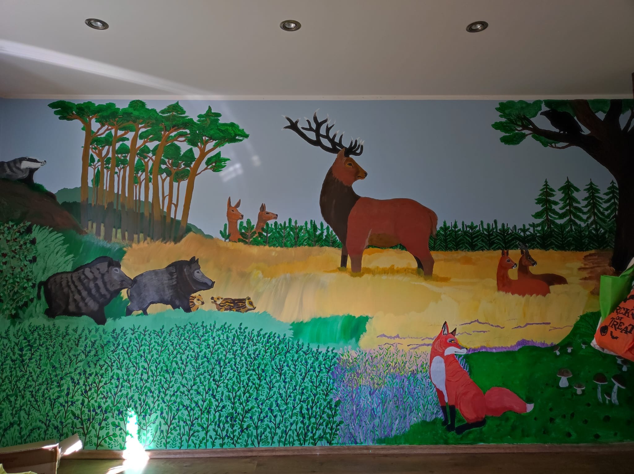 Ręcznie malowana ściana w pokoju dziecięcym z motywem leśnych zwierząt: jeleń, dziki, lis, borsuk, sarny i ptak na drzewie.