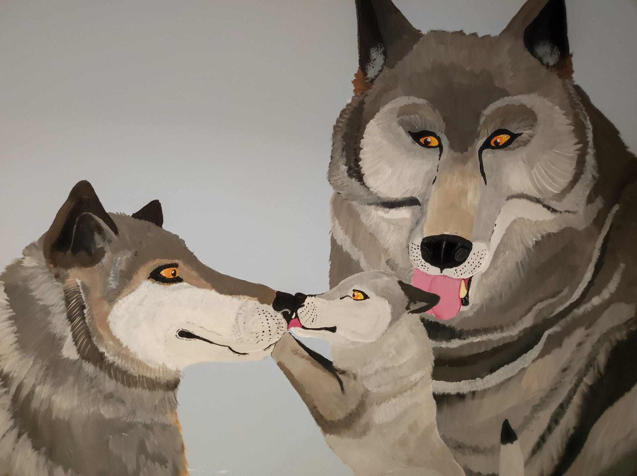 Akrylowy portret rodziny wilków: dorosły wilk, wilczyca i szczeniak, z szarobrązową sierścią i pomarańczowymi oczami, na gładkim, jasnoszarym tle ściany.