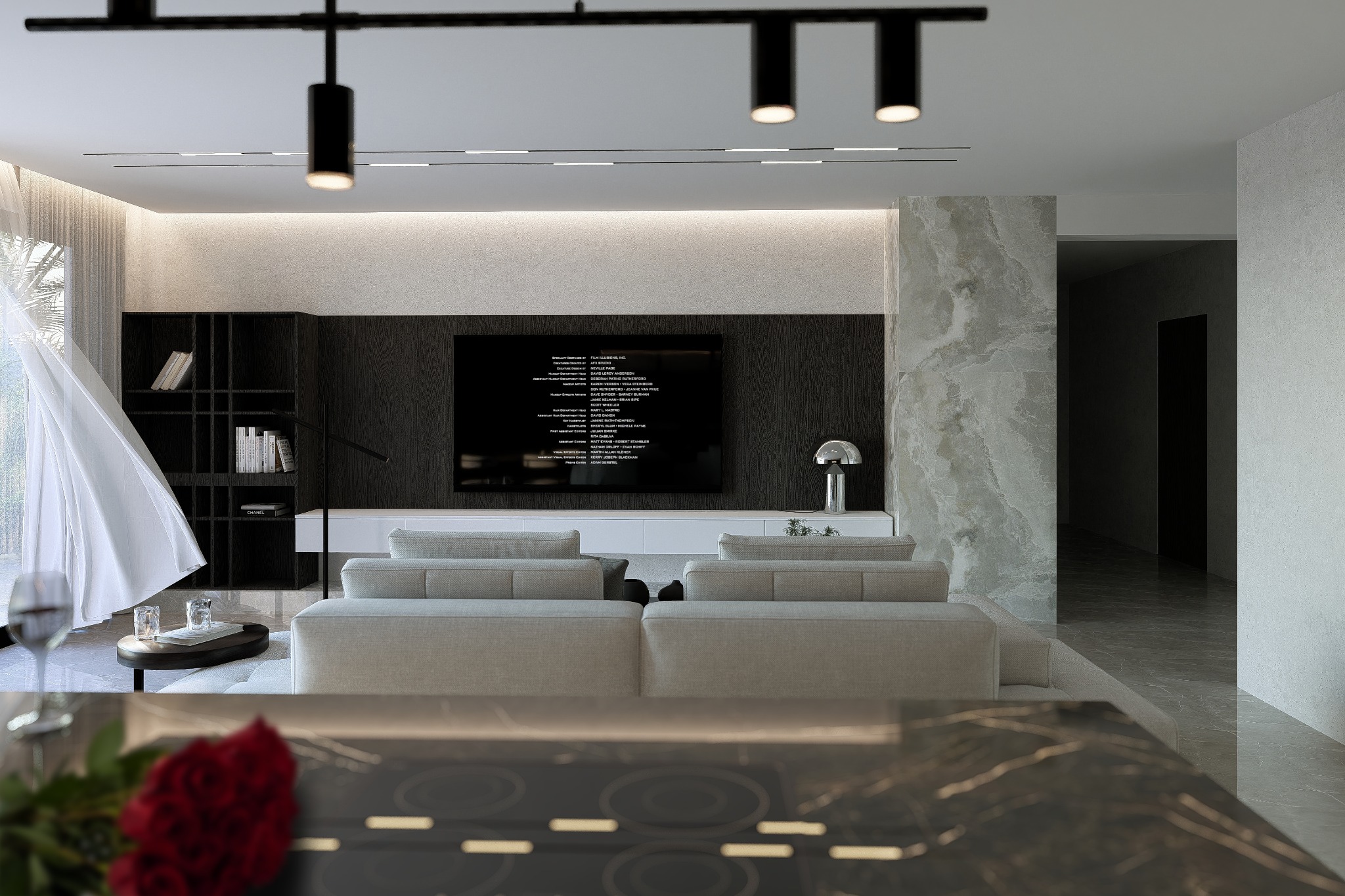 Elegancki salon z sofą modułową, czarną zabudową TV i marmurowymi akcentami. Widok z blatu kuchennego z bukietem czerwonych róż w pierwszym planie.