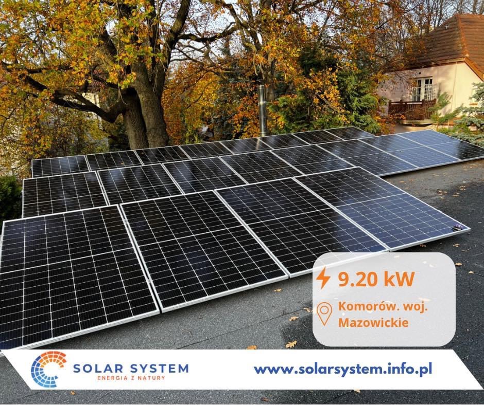 Instalacja paneli słonecznych na dachu domu jednorodzinnego, widok z góry, jesienne drzewa w tle, informacja o mocy 9.20 kW i lokalizacji Komorów, woj. Mazowieckie.