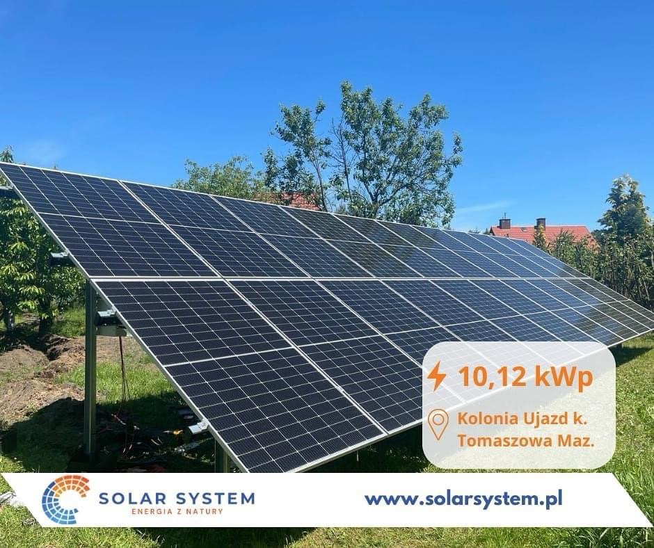 Panel słoneczny o mocy 10,12 kWp zainstalowany w Kolonii Ujazd koło Tomaszowa Mazowieckiego, widoczny na tle błękitnego nieba i zieleni drzew, z logo firmy Solar System.