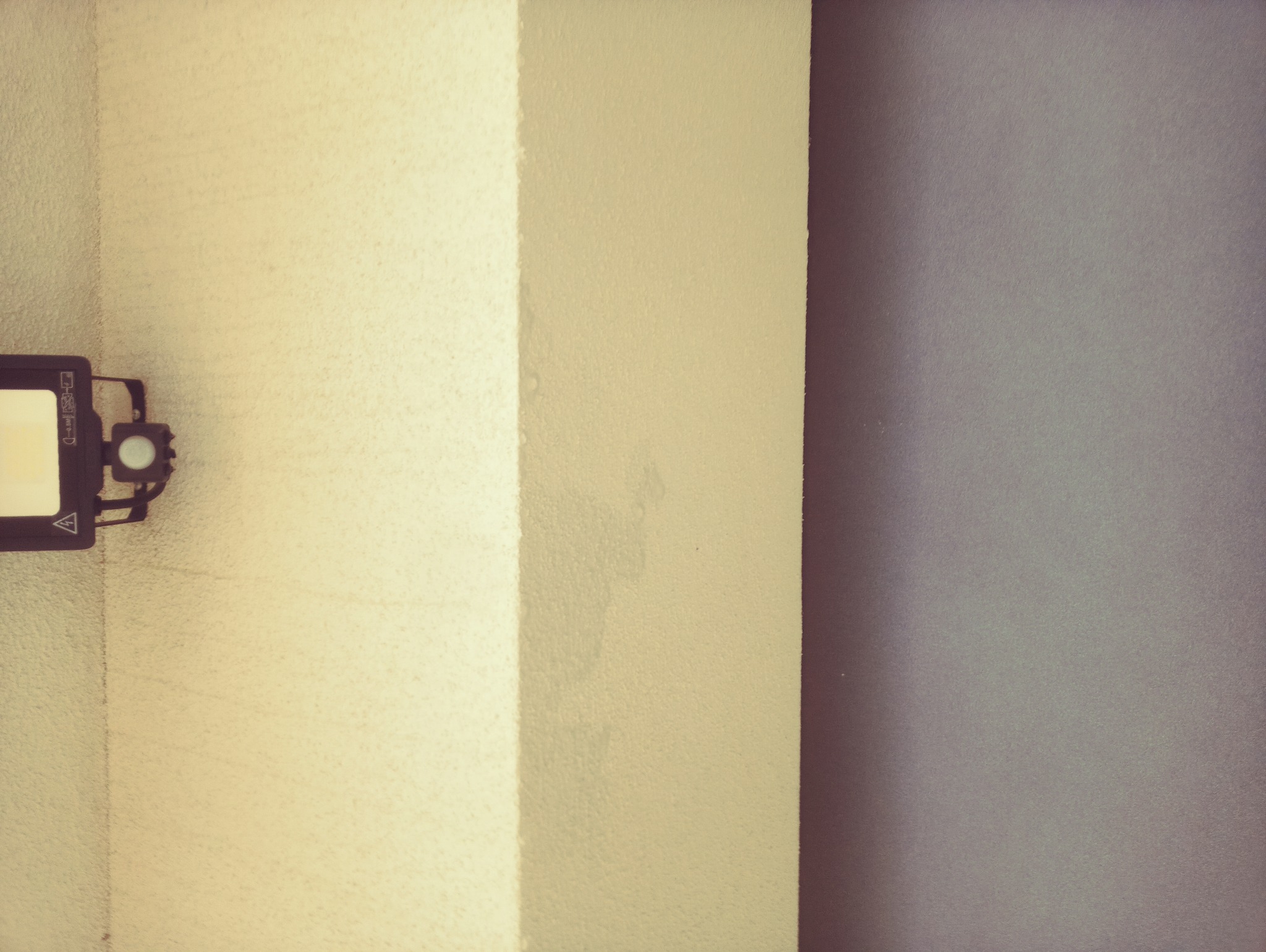 Nierównomiernie pomalowana ściana w odcieniach beżu i szarości, z widocznym fragmentem poziomicy laserowej po lewej stronie.
