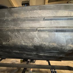 Spawanie Plastiku Zagrodzki - Spód czarnej łodzi lub kajaka z widocznymi śladami użytkowania i napraw, umieszczony na metalowym stojaku.