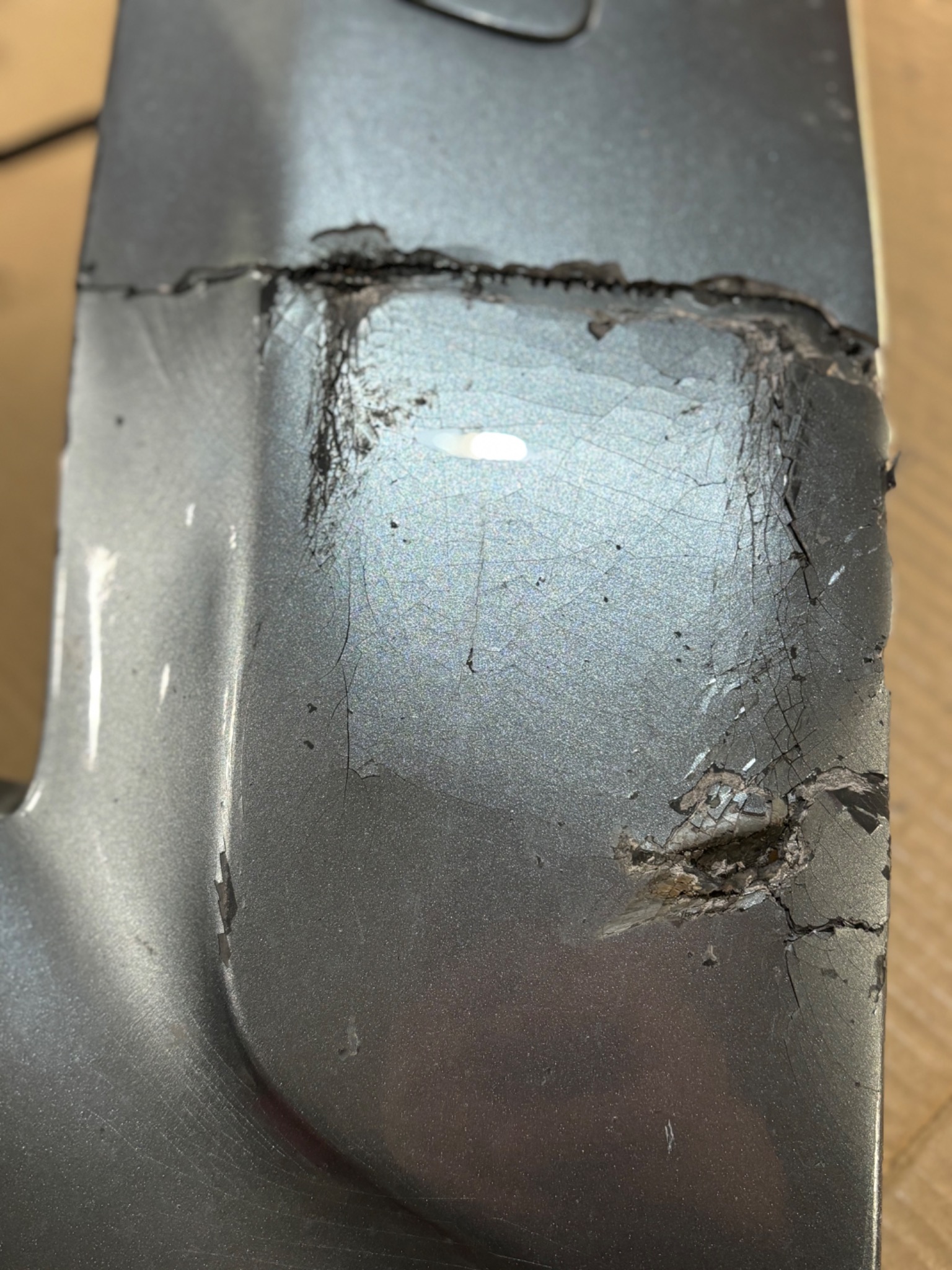 Uszkodzony, pęknięty i pospawany element metalowy z widocznymi śladami naprawy i ubytkami.