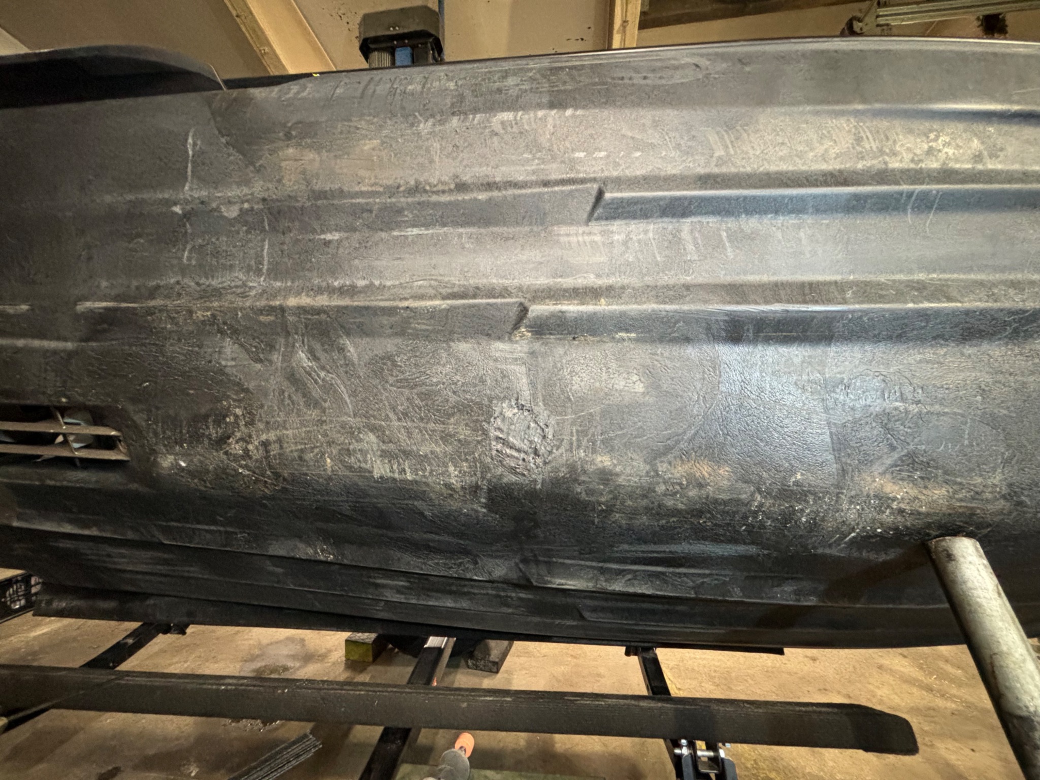 Spód czarnej łodzi lub kajaka z widocznymi śladami użytkowania i napraw, umieszczony na metalowym stojaku.