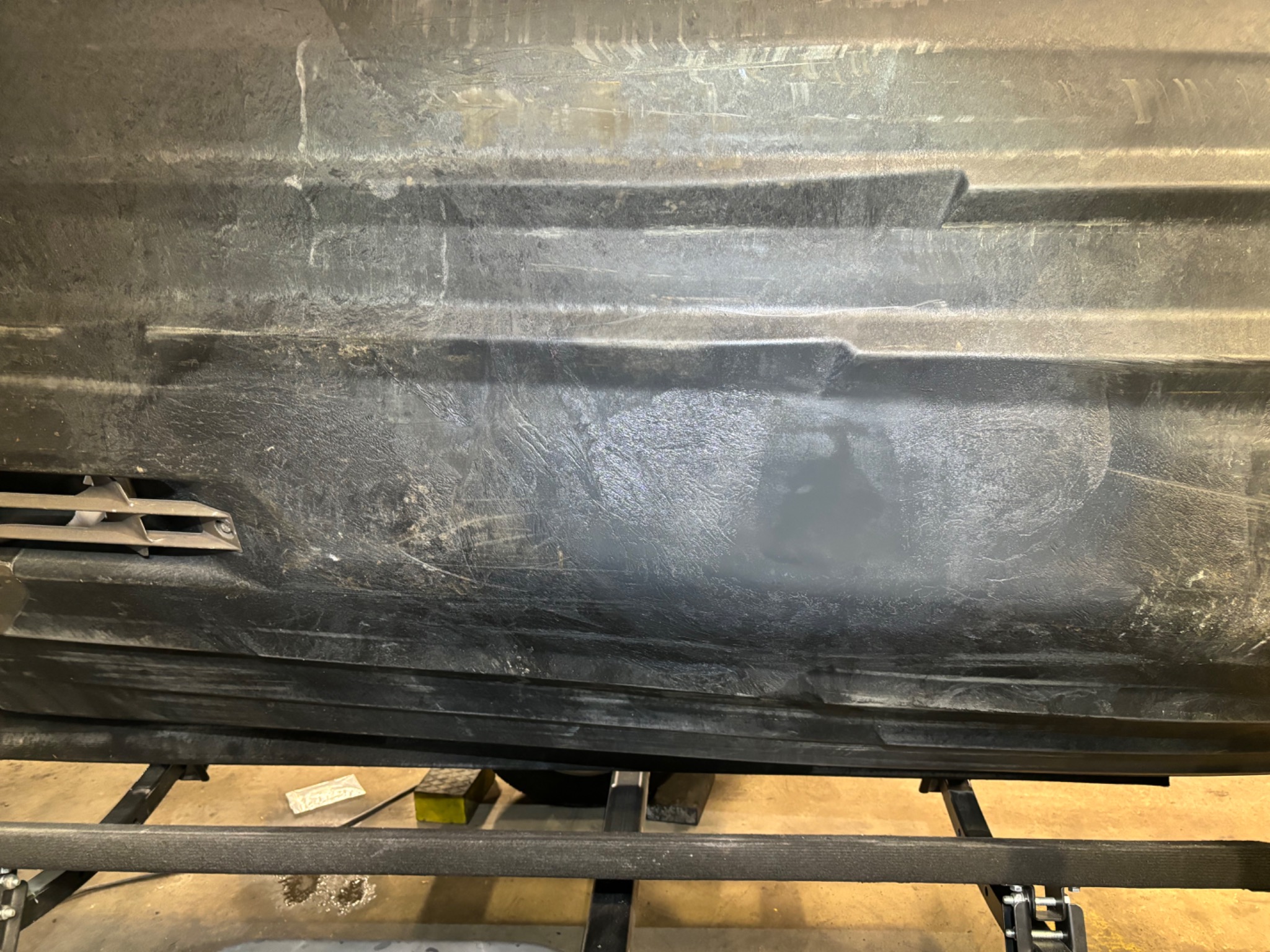 Spodnia część czarnej, plastikowej łodzi na metalowej przyczepie, widoczne ślady użytkowania i naprawy.