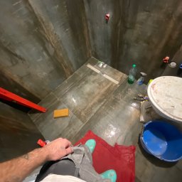 Yasnichenko Ihor Boroda_Bud - Ukończony prysznic z ciemnymi płytkami imitującymi drewno, widoczne narzędzia i akcesoria glazurnicze, w tym poziomica, gąbka, wiadro i zaprawa.