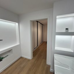 Boroda_Bud - Białe wnętrze z drewnianą podłogą, wnękami z oświetleniem LED i szafą w zabudowie. Minimalistyczny design, jasne kolory, nowoczesne wykończenie.