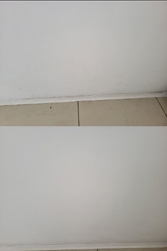 Biała ściana z widocznymi zabrudzeniami przy listwie przypodłogowej i brudnymi fugami w jasnych płytkach podłogowych, ukazująca stan przed czyszczeniem.