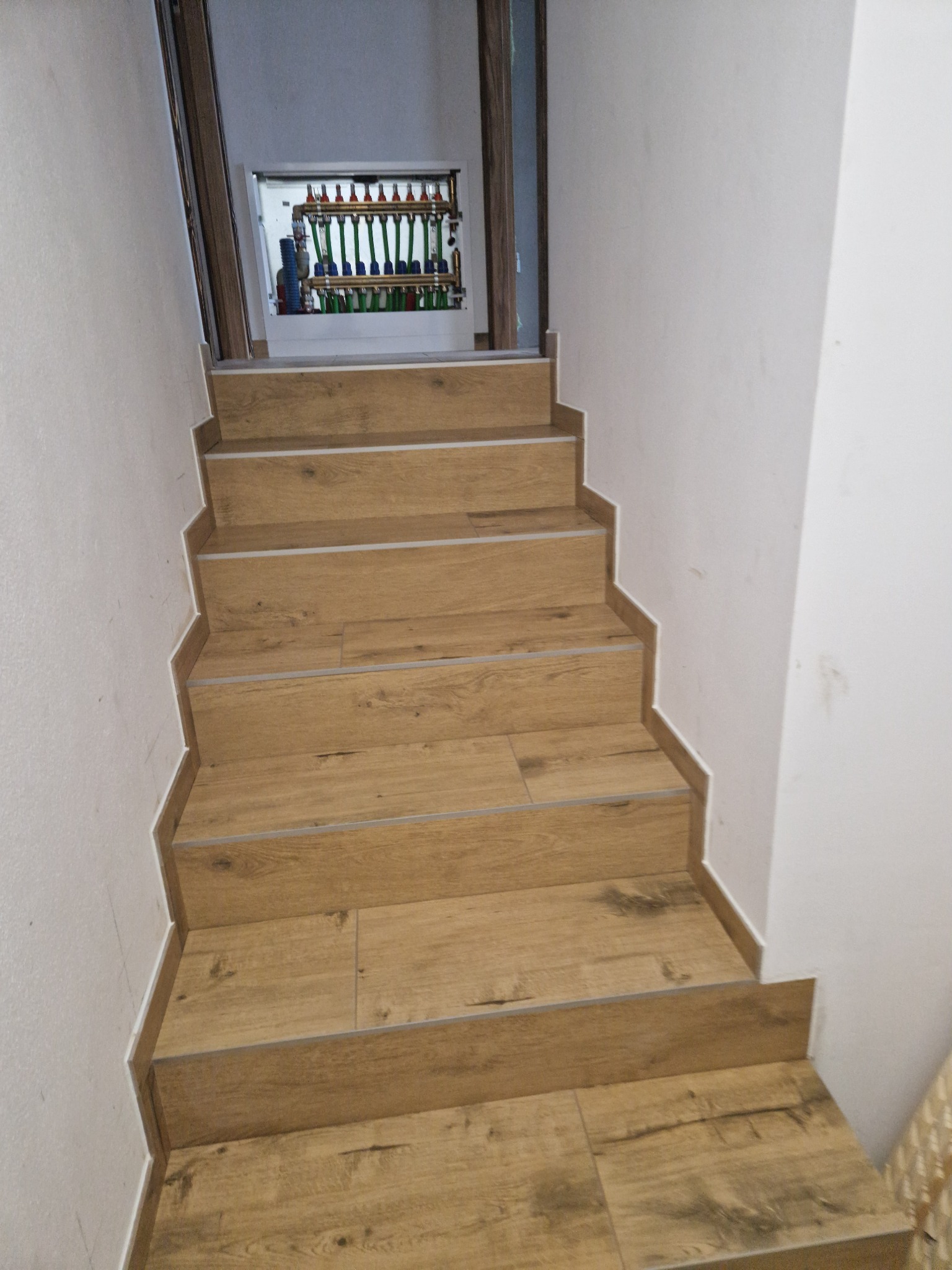 Schody wyłożone panelami imitującymi drewno, z widoczną instalacją ogrzewania podłogowego w tle.