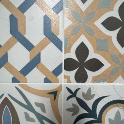 WallCraft-Remonty - Cztery płytki ceramiczne z różnymi wzorami geometrycznymi i kwiatowymi w odcieniach błękitu, szarości i beżu, z drobnymi zabrudzeniami na powierzchni.