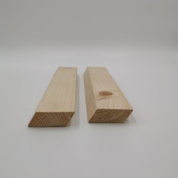 WOODPECKER PAULINA PŁOŃCZYK - Dwa kawałki świeżo obrobionego drewna iglastego, oba z ukośnie ściętym końcem, leżące na białym tle. Jeden kawałek ma widoczny sęk.