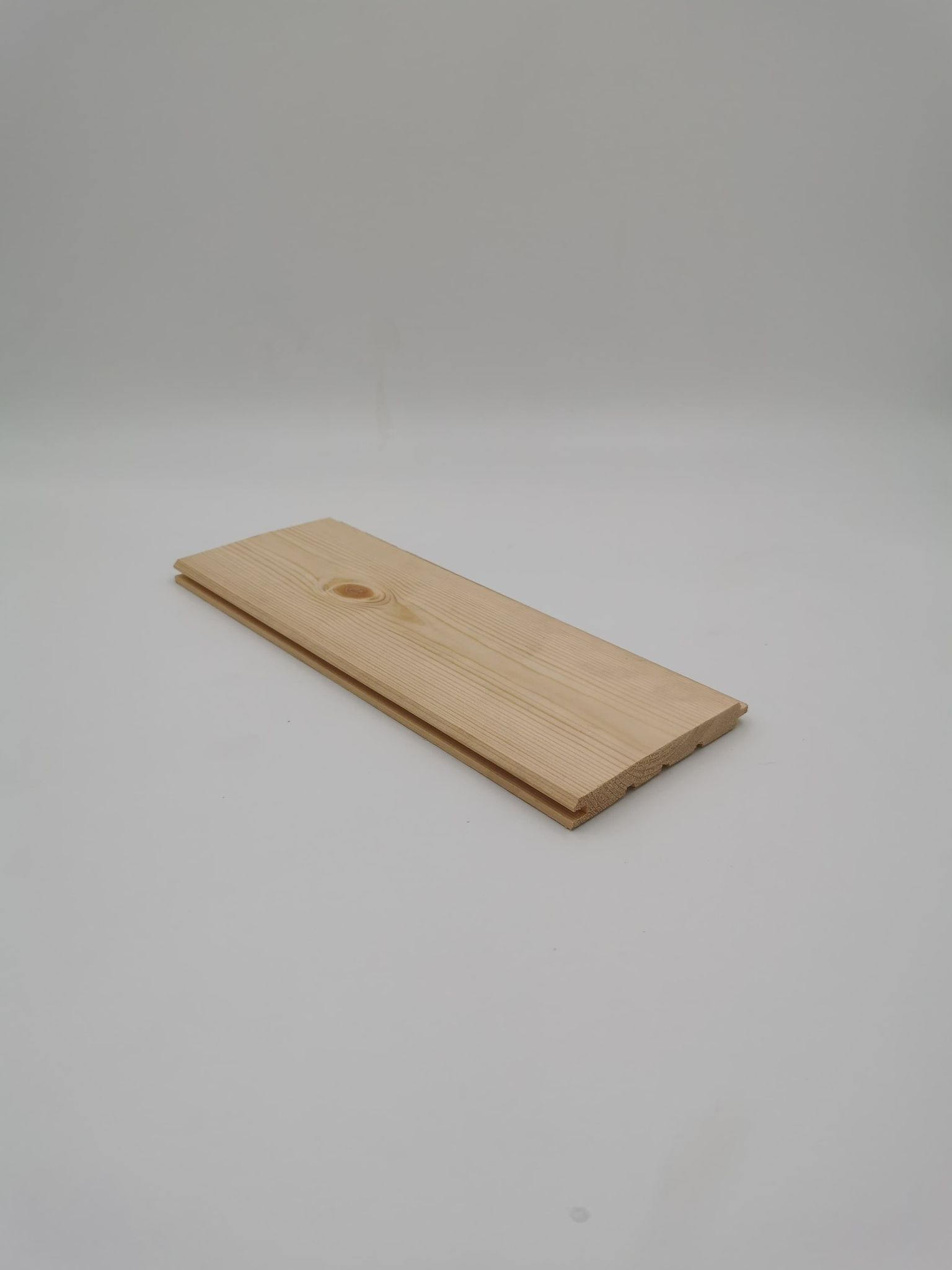 Profilowana deska z jasnego drewna z widocznym sękiem, ułożona na jasnym, jednolitym tle.