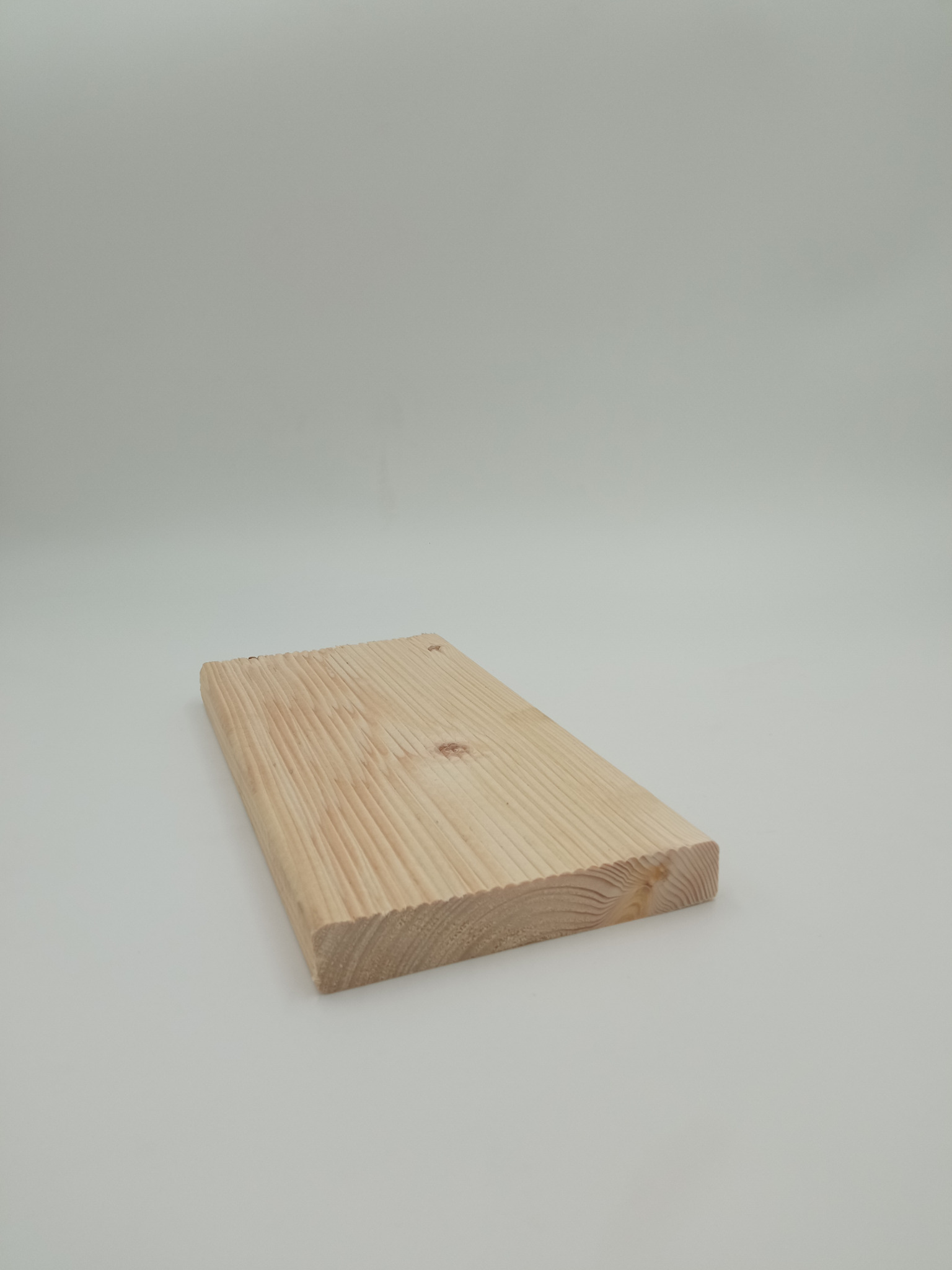 Surowa deska z jasnego drewna sosnowego, widoczne słoje i niewielkie sęki, leżąca na jednolitym, jasnoszarym tle.