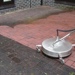 VitLen- Clean Olena Cherkashyna - Mycie kostki brukowej: fragment wyczyszczonej czerwonej kostki brukowej w jodełkę kontrastuje z brudną, ciemną częścią. Widoczna maszyna czyszcząca z dyszą.