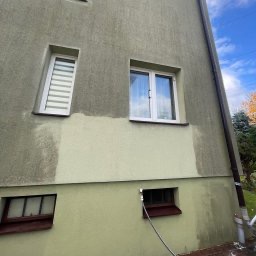 Fragment elewacji budynku po częściowym umyciu, widoczna różnica w kolorze, z przewodem ciśnieniowym u dołu. Ujęcie z dołu, niebo z chmurami w tle.