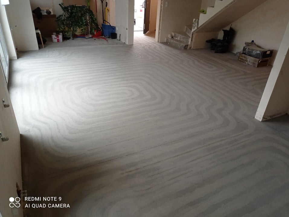 Przygotowany podkład pod ogrzewanie podłogowe w dużym pomieszczeniu, widoczne spiralne ułożenie rur grzewczych zalane wylewką, gotowe do dalszych prac wykończeniowych.