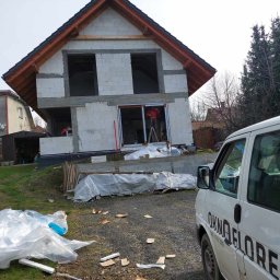 Okno Florek - drzwi, okna, rolety, bramy garażowe - Budowa domu jednorodzinnego w stanie surowym otwartym, widoczny montaż okna przez pracownika na drabinie, na pierwszym planie biały bus z napisem 'OKNO FLOREK'.