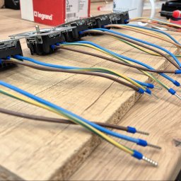 LVA Systems Aleksander Kociemba - Szereg modułów elektrycznych Legrand z podłączonymi kolorowymi przewodami, zakończonymi precyzyjnie zaciskniętymi tulejkami, na drewnianym blacie.
