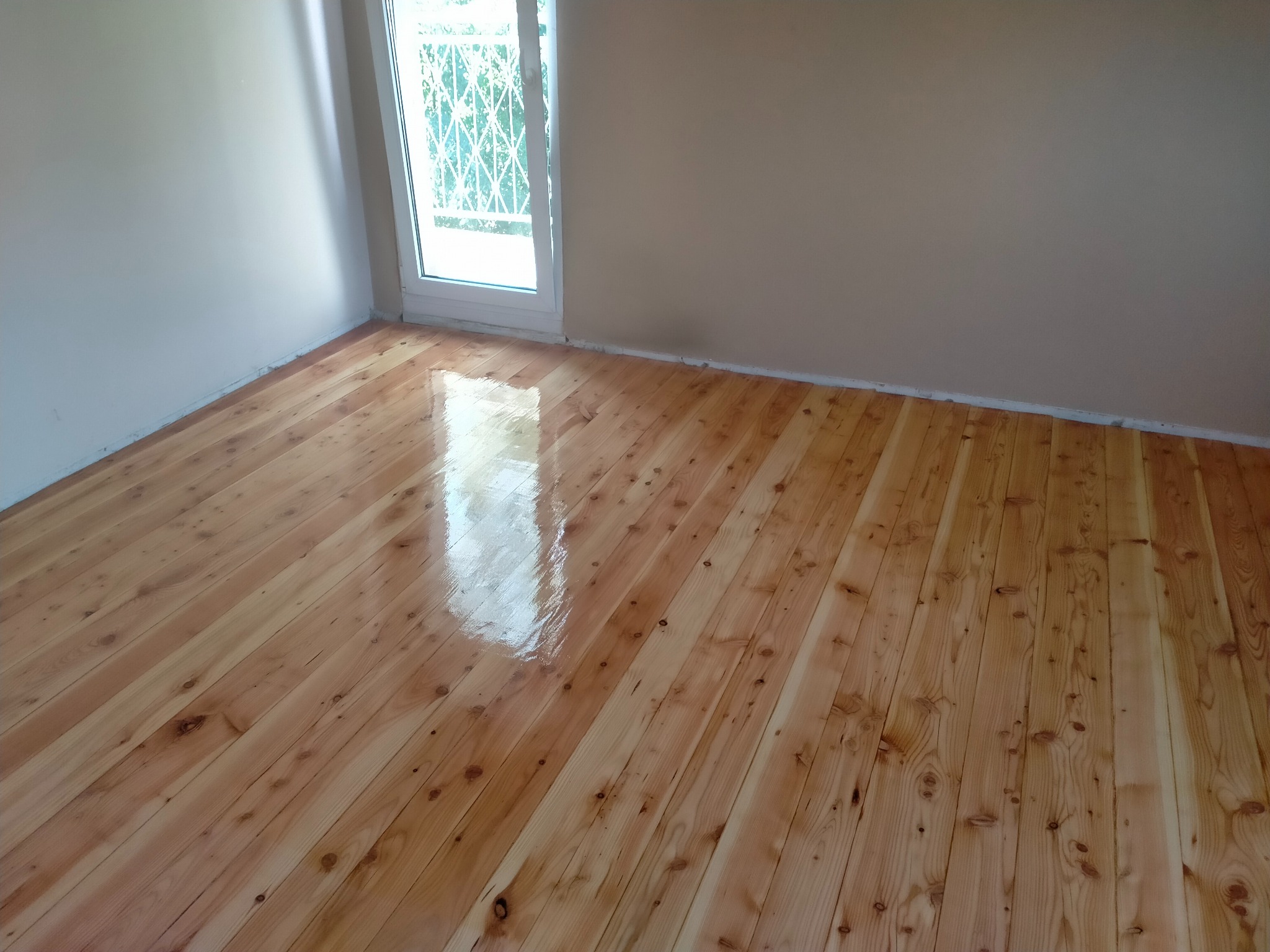 Błyszcząca, odnowiona drewniana podłoga z widocznym odbiciem światła z okna, świeżo po cyklinowaniu i lakierowaniu.