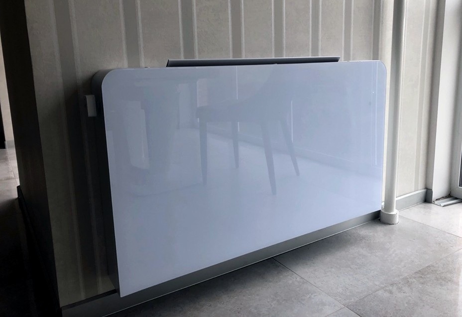 Zamknięta jednostka rekuperacyjna z białym panelem na ścianie z pionowymi paskami, widoczne odbicie krzesła.