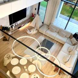 CUBE27 SPÓŁKA Z OGRANICZONĄ ODPOWIEDZIALNOŚCIĄ - Wnętrze domu z widokiem z góry: jadalnia z nakrytym stołem, salon z narożną sofą, pokój dziecięcy z tipi i zabawkami, duże okna z widokiem na ogród, nowoczesne oświetlenie w postaci okręgów.