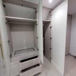 Shakira Monika Mathea - Jasna szafa z otwartymi drzwiami, widoczne półki, szuflady z złotymi uchwytami i ukryta garderoba. Dopasowana do skosów poddasza, nowoczesny design.