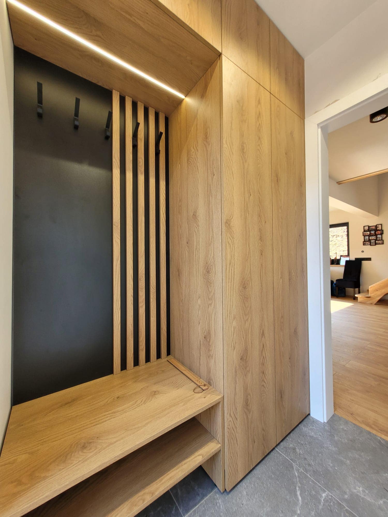 Nowoczesna szafa wnękowa z jasnego drewna z czarnym panelem i wieszakami, oświetlenie LED, widok na przedpokój z drewnianą podłogą.