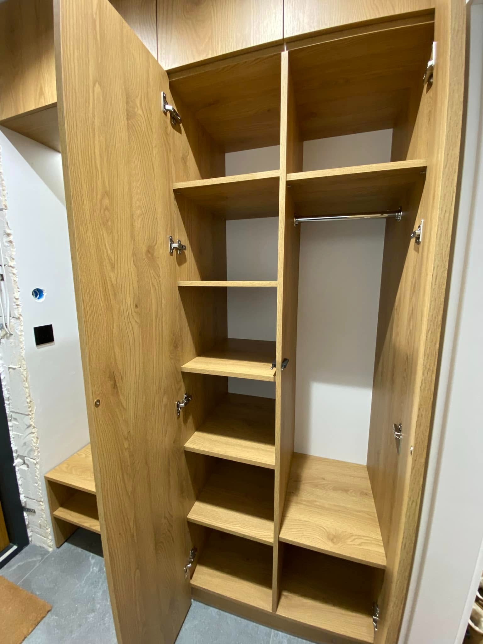 Otwarta, drewniana szafa wnękowa z półkami i drążkiem, widoczna w trakcie montażu, z niedokończonymi ścianami w tle.