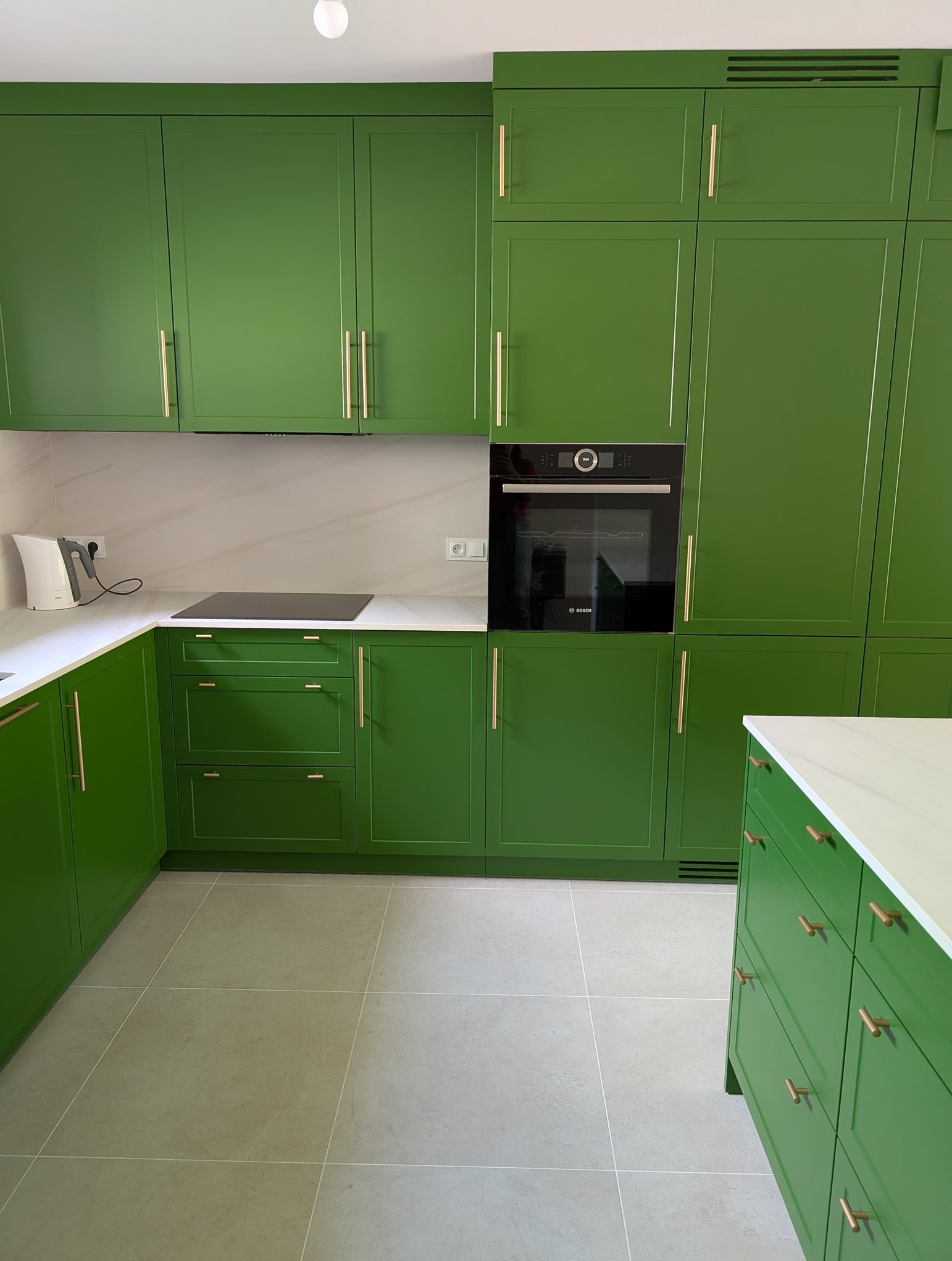 Zieleń paproci: angielska kuchnia z złotymi uchwytami. Zabudowa z piekarnikiem Bosch, biały blat i płytki podłogowe. Nowoczesny design, eleganckie wykończenie.