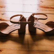 Para damskich, brokatowych, beżowych czółenek na niskim, klockowym obcasie, z paskiem wokół kostki, ułożona na drewnianej podłodze.