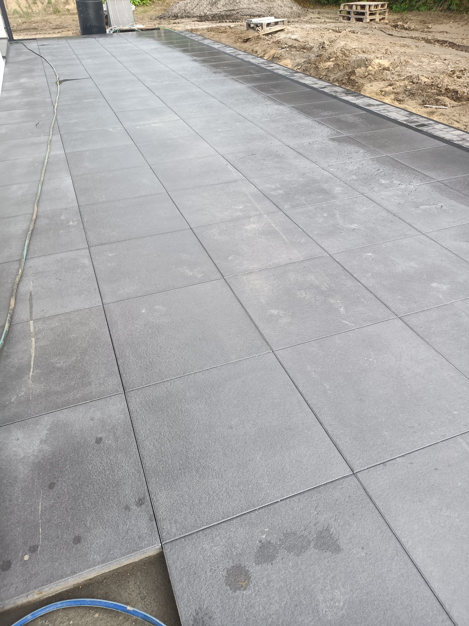 Nowoczesna, szara kostka brukowa ułożona na posesji w Żukowie. Widoczne równe linie i estetyczne wykończenie obrzeży. Część terenu jeszcze w trakcie prac ziemnych.