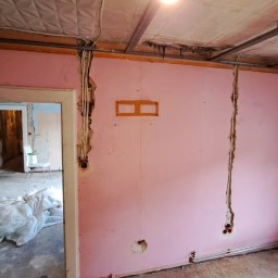 ETB Tomasz Bieniasz - Różowy pokój w trakcie remontu z widocznymi bruzdami w ścianie przygotowanymi pod przewody elektryczne, odsłonięta instalacja elektryczna w ścianie, fragment podwieszanego sufitu z widocznymi...